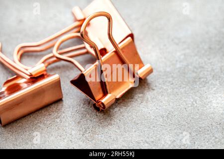 Roségoldfarbene kupferfarbene Büroklammern auf meliertem Grau Stockfoto