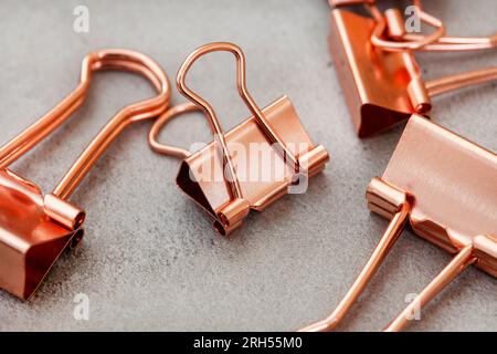 Roségoldfarbene kupferfarbene Büroklammern auf meliertem Grau Stockfoto