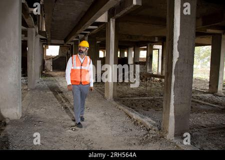Junger indischer Bauingenieur oder Architekt, der Helm und Weste trägt und auf der Baustelle inspiziert. Volltreffer. Stockfoto