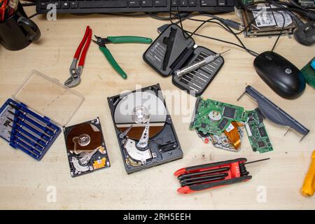 Arbeitstisch für Elektroniktechniker mit Handwerkzeugen und Computerkomponenten, darunter zwei offene Festplatten. Stockfoto