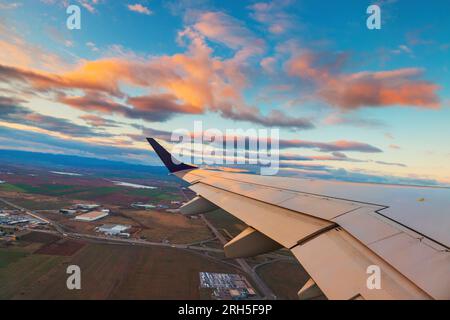 Flugzeugflug bei Sonnenuntergang über der Stadt und im Flügel des Flugzeugs. Blick vom Fenster des Flugzeugs. Reisen in der Luft. Stockfoto