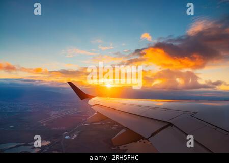 Flugzeugflug bei Sonnenuntergang über der Stadt und im Flügel des Flugzeugs. Blick vom Fenster des Flugzeugs. Reisen in der Luft. Stockfoto