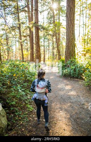 Rückansicht einer Mutter, die ein Kleinkind trägt, beim Wandern im Wald Stockfoto