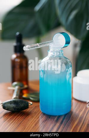 Ätherisches Aromaöl oder Serumessenz in blauen Glasflaschen auf einem Holztisch vor dem Hintergrund grüner Pflanzen und Schönheitsprodukte. Konzept von cos Stockfoto
