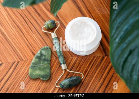 Gouache-Rolle und Stein mit Gesichtscreme auf hölzernem Hintergrund, Draufsicht. Hautpflegekonzept Stockfoto