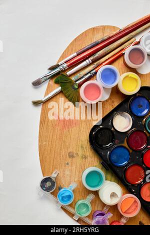 Flachlagerung von bunten Farben, Malerpalette und Pinseln auf weißem Hintergrund, Kunst, Malen und Hobbykonzept, Draufsicht, Kopierbereich. Stockfoto