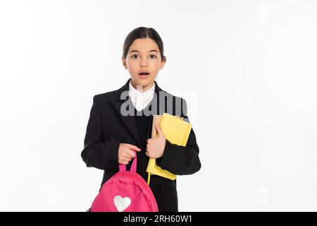 Schockiertes Schulmädchen, das mit Notebooks und Rucksack auf Weiß steht, das Konzept für den Schulanfang Stockfoto