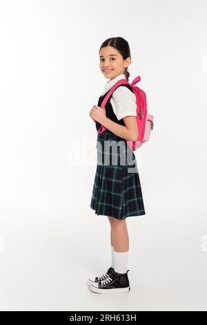 Durchgehendes, glückliches Schulmädchen in Uniform mit Rucksack auf Weiß, bereit für das neue Schuljahr Stockfoto