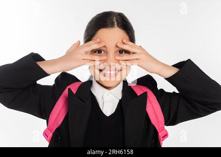 Glückliches Schulmädchen in Uniform, das Augen verdeckt, isoliert auf weißes Studentenleben, in die Kamera schaut Stockfoto
