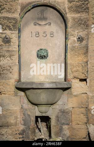 Viktorianischer Trinkbrunnen aus dem Jahr 1858 in Belper Derbyshire, England, mit Löwenkopf-Wasserhahn. Der Brunnen ist in die ältere Gangway Bridge von 1795 eingebaut Stockfoto