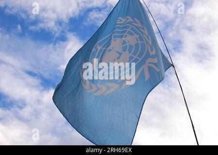 Hintergrundbeleuchtete UN-Flagge, die im Wind winkt. Offizielles Emblem der Vereinten Nationen. Konzept für den Weltfrieden Stockfoto