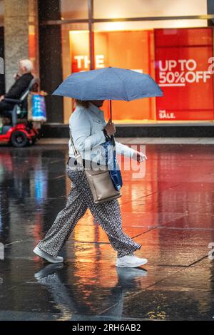 Southport, Merseyside. Wetter in Großbritannien. 14. August 2023; Wetter in Großbritannien. Um 19C Uhr regnet es warm, während die Käufer in Southport nass werden. Ausbrüche von Regenschauern in Nordengland und Wales heute Nachmittag, heftig und donnernd an einigen Stellen. Schwankende Wolken, sonnige Zauber und verstreute Schauer im Nordwesten. Kredit; MediaWorldImages/AlamyLiveNews Stockfoto