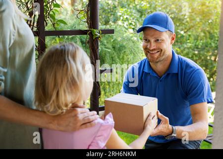 Mutter mit Kind nimmt ein Lieferpaket von einem lächelnden Liefermann an der Haustür an Stockfoto