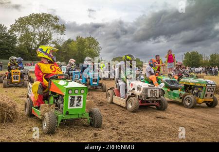 Die Fahrer sitzen auf ihren Rasenmähern, während sie auf die Zuweisung von Startpositionen im jährlichen britischen Rasenmäherrennen im Le Mans-Stil warten Stockfoto