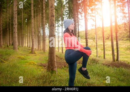 Sportliche Frau, die Beindehnungsübungen macht, draußen im Wald. Outdoor-Trainingskonzept. Stockfoto