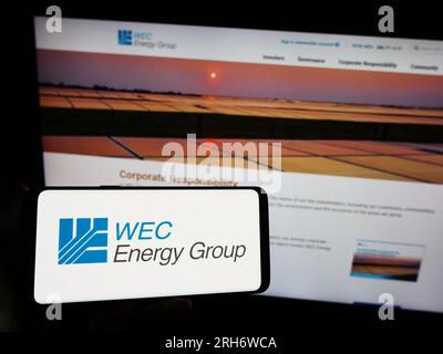 Person, die ein Mobiltelefon mit dem Logo des amerikanischen Versorgungsunternehmens WEC Energy Group Inc. Auf dem Bildschirm vor der Webseite hält. Konzentrieren Sie sich auf das Display des Telefons. Stockfoto