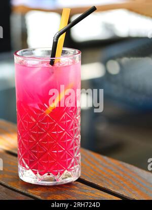 Himbeereistee. Ein Glas Himbeerlimonade mit Zitrone und Eiswürfeln. Kalter erfrischender rosafarbener Cocktail in einem hohen Kristallglas auf einem hölzernen Restaurant Stockfoto