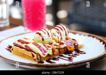 Belgische Waffeln mit Eis, Beerensauce und frischen Obstscheiben auf einem Teller auf einem Restauranttisch. Nahaufnahme von Vollkornmehl belgischer Waffel mit Stockfoto