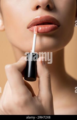 Schnittbild einer jungen Frau, die Lipgloss aufträgt, während sie sich beige isoliert schminkt Stockfoto
