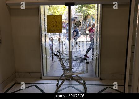 Zerbrochenes Glas an der Eingangstür des Supermarkts. Moderne, modische gepanzerte Glastür in einem Netz aus Rissen nach einem Akt des Vandalismus während des Krieges. Stockfoto