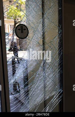 Zerbrochenes Glas an der Eingangstür des Supermarkts. Moderne, modische gepanzerte Glastür in einem Netz aus Rissen nach einem Akt des Vandalismus während des Krieges. Stockfoto