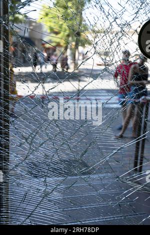 Zerbrochenes Glas an der Eingangstür des Supermarkts. Moderne, modische gepanzerte Glastür in einem Netz aus Rissen nach einem Akt des Vandalismus während des Krieges. Stockfoto