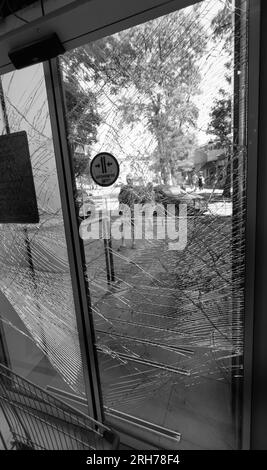 Zerbrochenes Glas an der Eingangstür des Supermarkts. Moderne, modische gepanzerte Glastür in einem Netz aus Rissen nach einem Akt des Vandalismus während des Krieges. Stockfoto