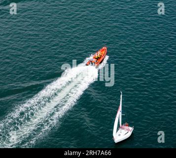 Luftaufnahme eines aufblasbaren Rettungsboots, das an einer kleinen Segelyacht vorbeifährt Stockfoto