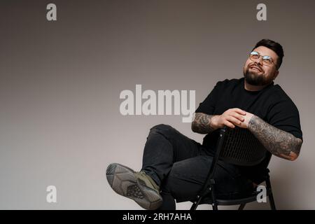 Bärtiger und tätowierter Mann, der im Studio auf einem Stuhl sitzt Stockfoto