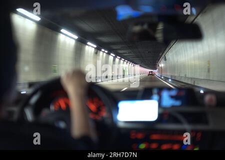 Blick auf das Innere des Fahrzeugs, das sich im Straßentunnel bewegt. Ein verschwommenes Armaturenbrett und eine Mädchenhand am Lenkrad. Die Schweiz Stockfoto