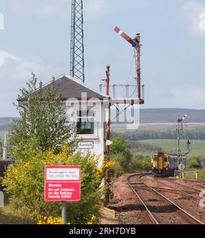 Der ScotRail-Sprinter der Klasse 156 überquert das mechanische Stellwerk und das Semaphore-Signal der hohen Halterung in New Cumnock, Ayrshire, Schottland, Großbritannien Stockfoto