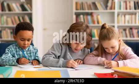 Aufmerksame multiethnische Schüler, Jungen und Mädchen, die einen Test schreiben, sitzen am Schreibtisch in der Grundschule, Panorama Stockfoto