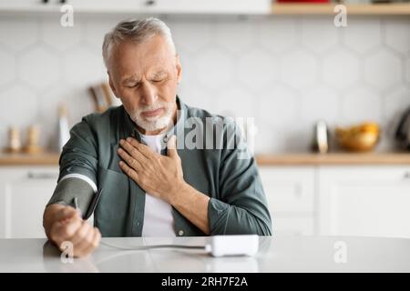 Senior Man Fühlt Sich Zu Hause Unwohl, Blutdruckmessung Mit Armmonitor Stockfoto