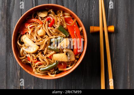 Teller mit Buchweizennudeln mit Gemüse, Pilzen, Hühnerfleisch auf dunklem Hintergrund, chinesische Stäbchen auf Holzhintergrund. Stockfoto