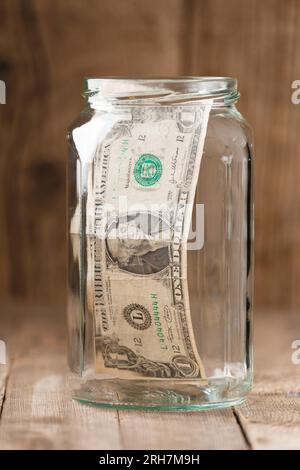 Eine-Dollar-Banknote in einem Glasbehälter auf einem Holzhintergrund, das Konzept von Sparen, Geldreserven, Finanzinvestitionen, Bargeldakkumulation. Stockfoto
