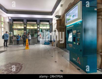 Fahrkartenschalter des Bahnhofs Lancaster mit einem Fahrgast, der ein Ticket kauft, andere stehen in der Warteschlange und niemand benutzt den Fahrkartenautomaten Stockfoto