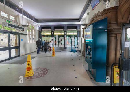 Fahrkartenschalter des Bahnhofs Lancaster mit einem Fahrgast, der ein Ticket kauft, andere stehen in der Warteschlange und niemand benutzt den Fahrkartenautomaten Stockfoto