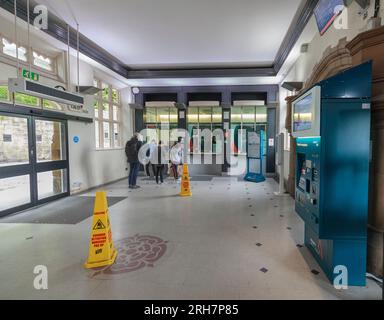 Fahrkartenschalter des Bahnhofs Lancaster mit einem Fahrgast, der ein Ticket kauft, andere stehen in der Warteschlange und niemand benutzt den Fahrkartenautomaten Stockfoto