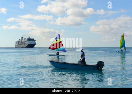 Segelboot in Pirates Cove bei Half Moon Cay, mit Holland America Line Kreuzfahrtschiff in der Ferne, Little San Salvador Island, den Bahamas. Stockfoto