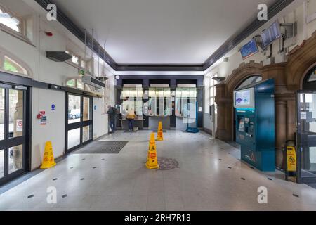 Fahrkartenschalter des Bahnhofs Lancaster mit einem Fahrgast, der ein Ticket kauft, andere stehen in der Warteschlange und niemand benutzt den Fahrkartenautomaten Stockfoto