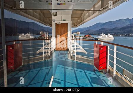 Reflexion über das Fenster des Kreuzfahrtschiffes Carnival Luminosa, verankertes Kreuzfahrtschiff und Hafen, mit Juneau Küste in der Ferne, Alaska. Stockfoto