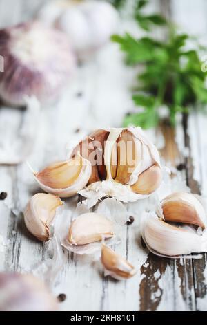 Nahaufnahme roter Inchelium-Knoblauchzehen auf weißem Holztisch mit Knoblauchzwiebeln im Hintergrund. Selektiver Fokus mit verschwommenem Vorder- und Hintergrund. Stockfoto