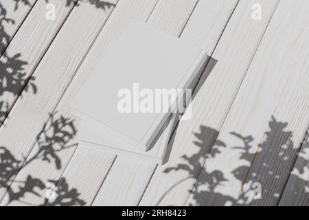Leeres Whitepaper für Ihr Design. Modell von zwei vergrabenen leeren Büchern auf weißem Holzhintergrund, Draufsicht. Buchlayout, Notizblock. 3D-Rendering. Stockfoto
