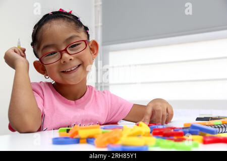 4-jähriges braunes Latina-Mädchen mit Autismus-Spektrum-Störung ASD wie Asperger, Rett und Heller zeichnet an einem Schreibtisch, spielt mit Farben allein, unsozial Stockfoto