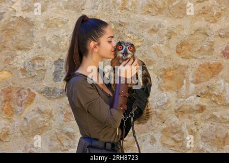 Eine Falknerin, die einen jungen Eurasischen Uhu mit großen schönen orangen Augen auf der Golubac-Festung in Golubac, Serbien, küsst Stockfoto