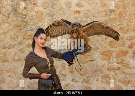 Eine Falknerin, die einen jungen Eurasischen Uhu mit großen schönen orangen Augen in der Golubac-Festung in Golubac, Serbien, hält Stockfoto