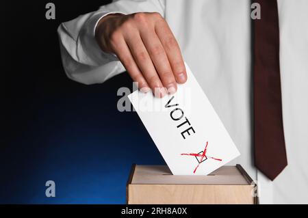 Ein Mann, der Papier mit Wortwahl und Haken in die Wahlurnen auf dunkelblauem Hintergrund legt Stockfoto