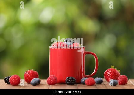 Becher mit verschiedenen frischen, reifen Beeren auf einem Holztisch im Freien Stockfoto