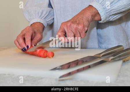 Eine ältere Frau schneidet Karotten auf einem Schneidebrett. Stockfoto