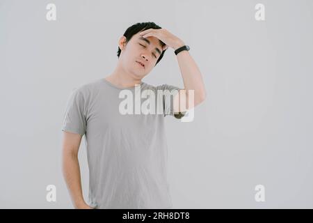 Selektive Fokussierung eines jungen Asiaten mit einem salbeigrünen lässigen T-Shirt und Smartwatch hatte Kopfschmerzen und hielt seinen Kopf mit der Hand auf isoliertem weißem B Stockfoto